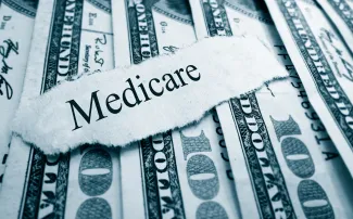PROMO HIRES Finance - Government Medicare Words Budget Money Cash - zimmytws - iStock-527631529 A scrap of torn paper with the word "Medicare" rests on top of a spread of United States 100 dollar currency.