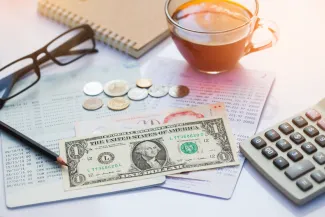 PROMO HIRES Finance - Money Dollar Calculator Glasses Statement Bank - iStock - Mamphotography Financial statement with assorted United States currency and coins, calculator, eyeglasses, and a cup of coffee on top.