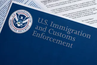 Overhead closeup of documents. The top document is entitled "U.S. Immigration and Customs Enforcement" with the United States Department of Homeland Security logo.