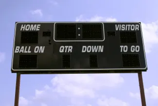 Football scoreboard in the foreground against a partly cloudy sky.