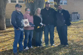 A group of people pose for a photo holding folded Colorado and United States flags