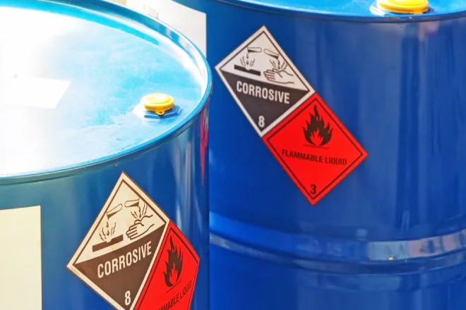 Two blue hazardous chemical barrels near each other. They both have warning labels for flammable and corrosive materials.