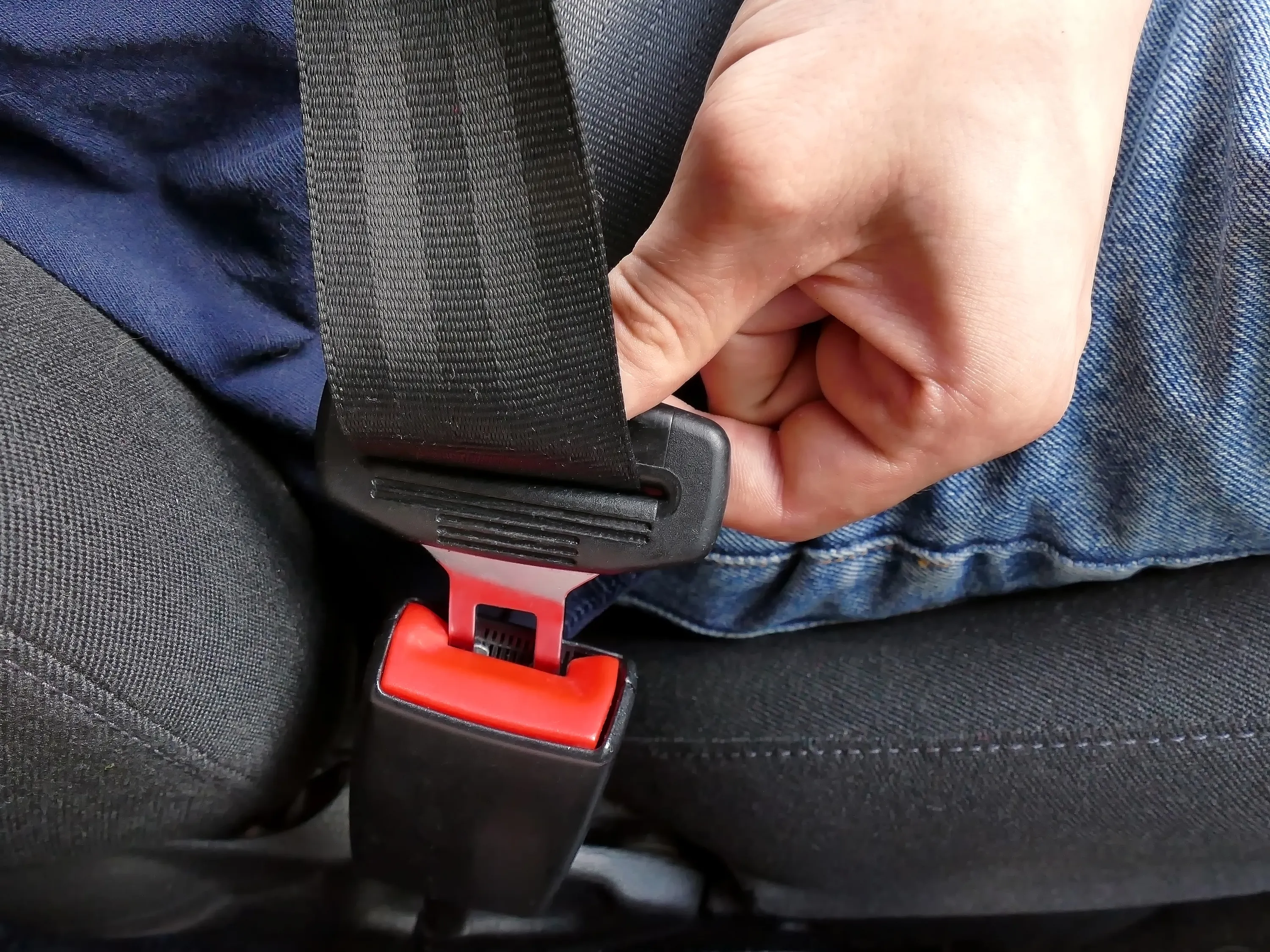 Closeup of a hand fastening a seat belt in a vehicle.