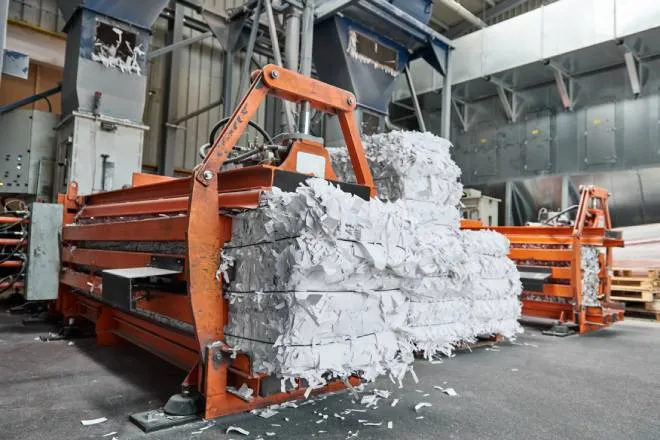 A large, orange-colored machine creates bales of shredded paper that are destined to be pulped and recycled.