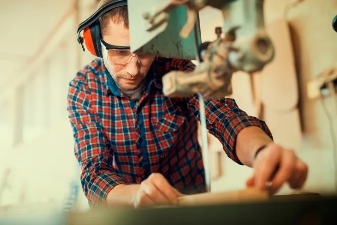 A bandsaw operator making a close cut and wearing proper safety gear such as headphones and eye protection.