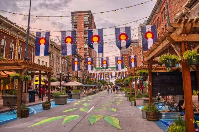 A downtown square in Colorado featuring road chalk art and hanging banners of the state flag symbol.