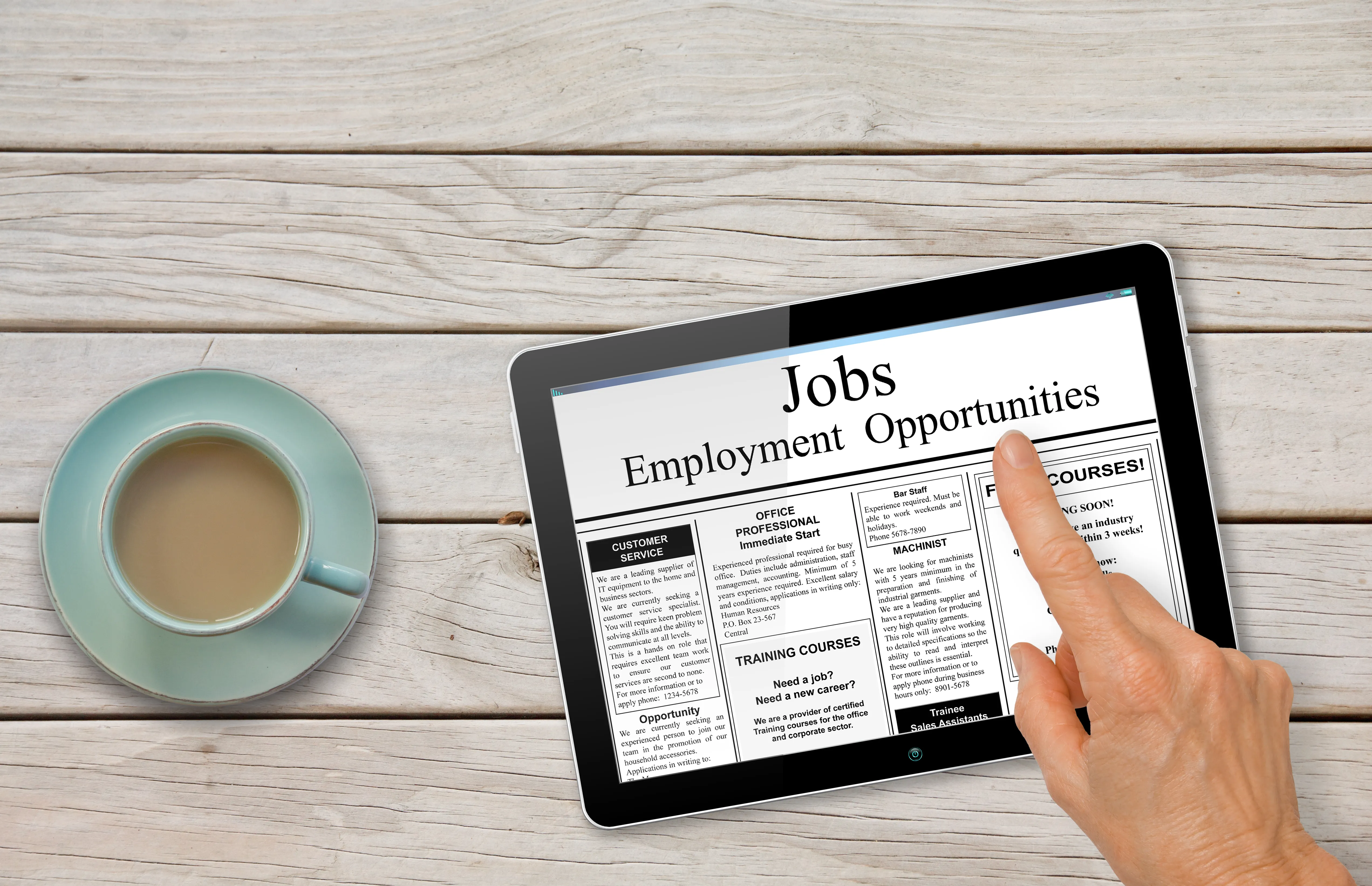 Tablet on a table next to a cup of coffee with the words "Jobs - Employment Opportunities." A hand hovers over the tablet.