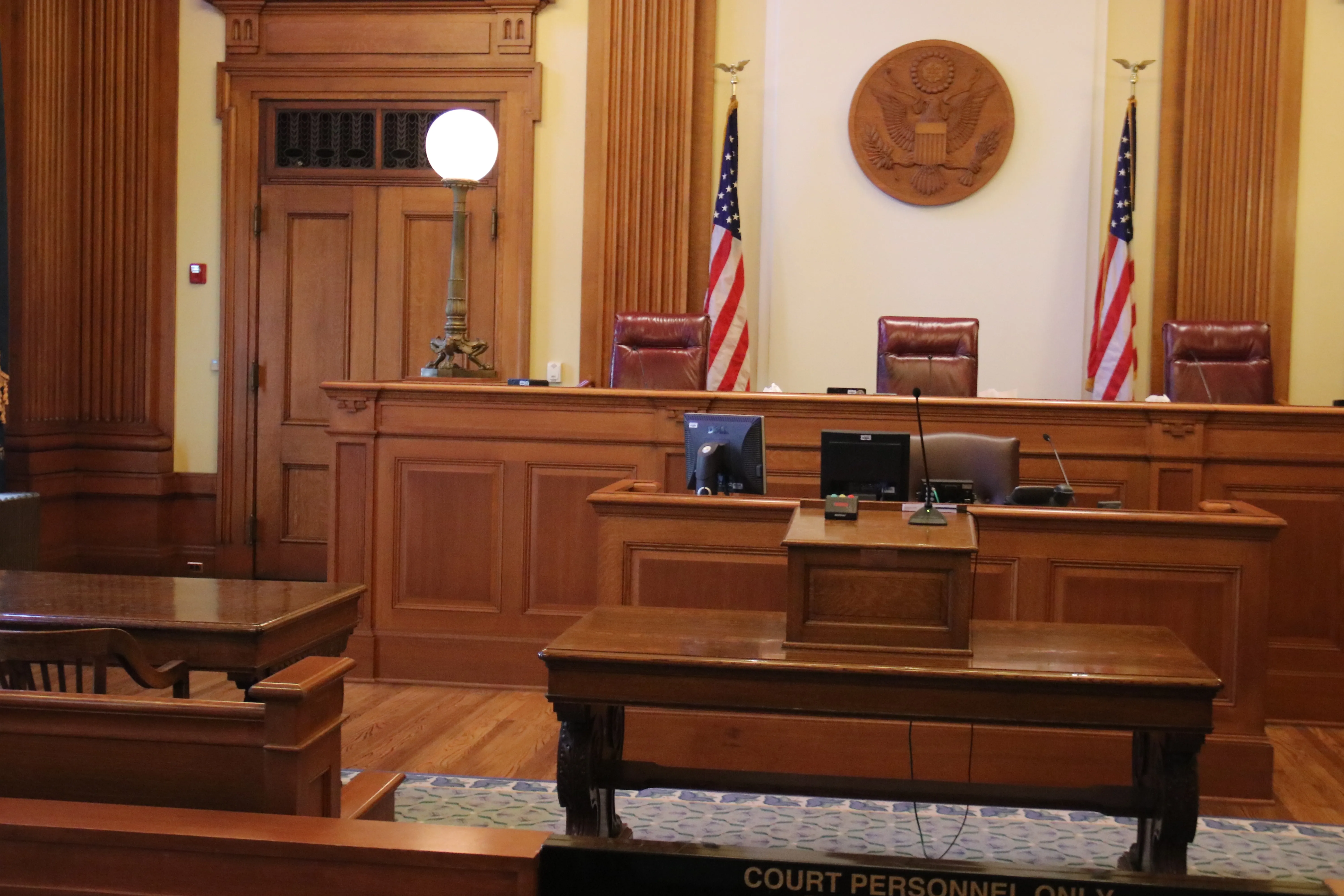 Scene of a courtroom facing the judges' bench flanked by two United States flags