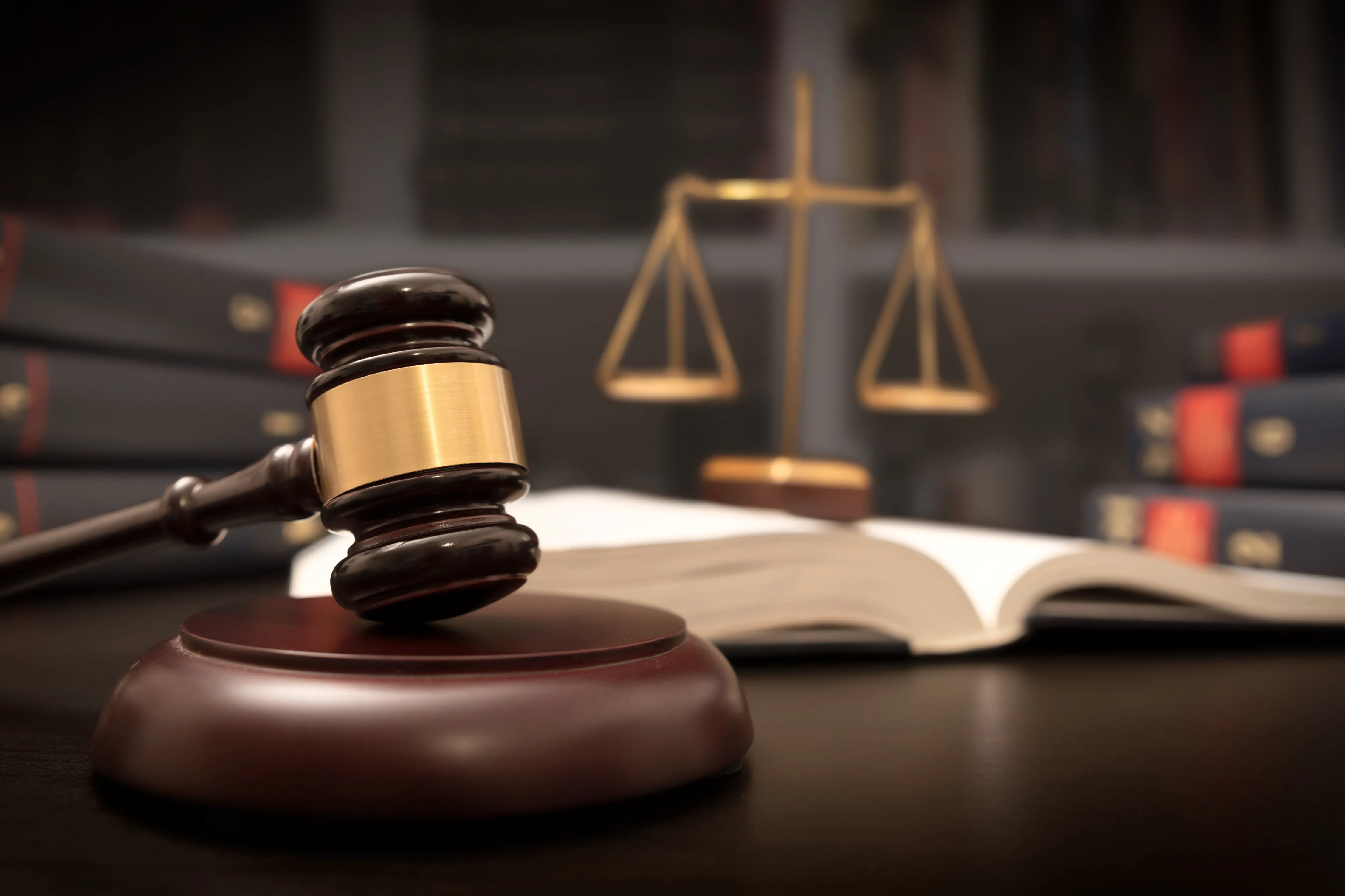 Court gavel on a strike plate, with the Scales of Justice and books in the background