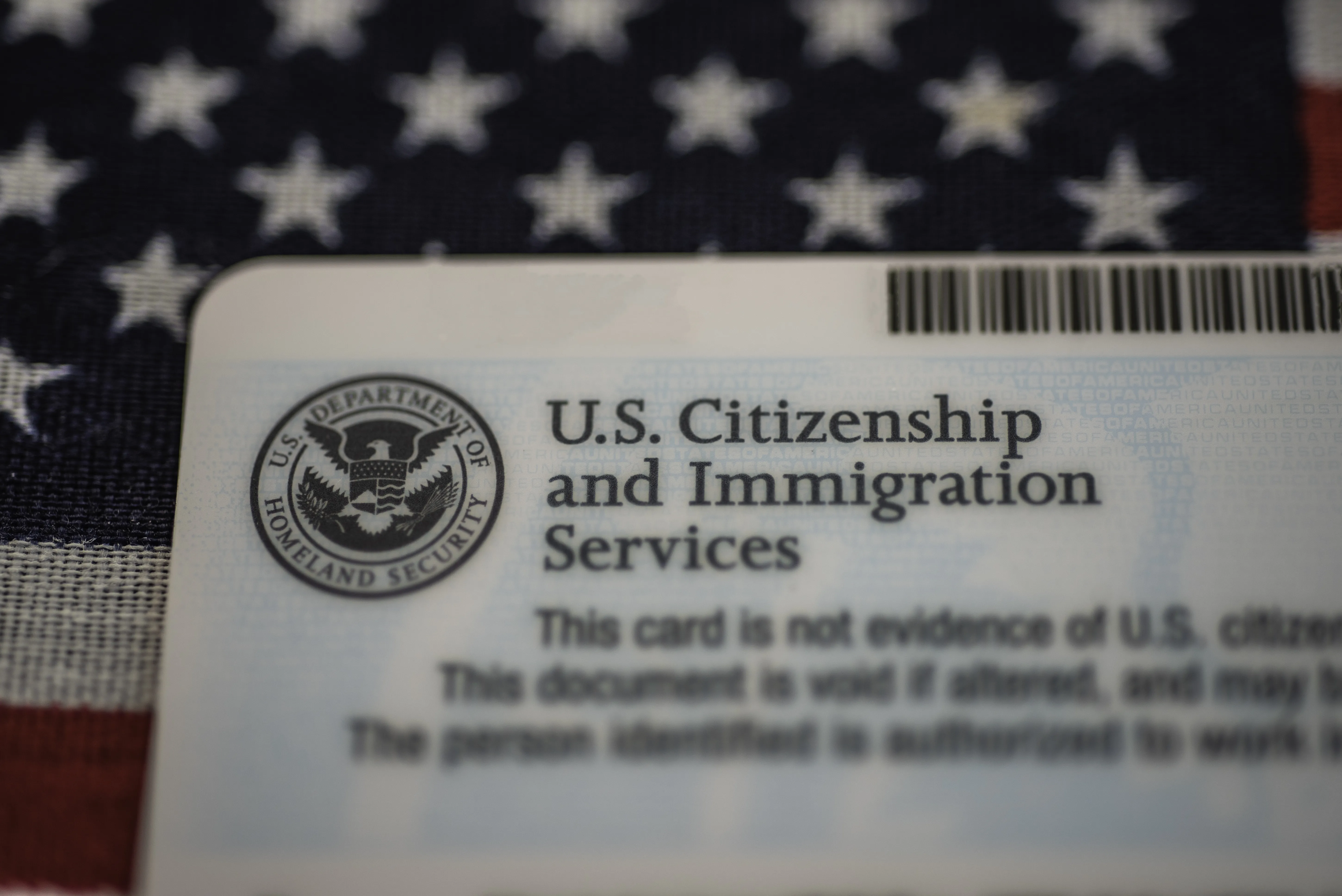 Closeup of a United States Citizenship and Immigration Services card. A United Sates flag is in the background.