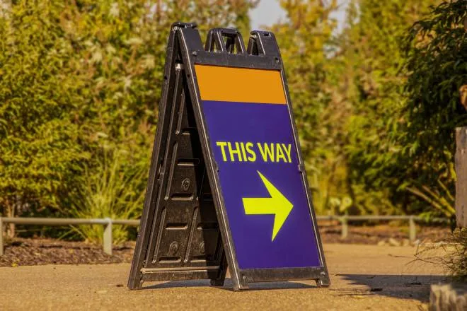 A large blue and orange A-frame sign with a printed message in yellow that says "THIS WAY" and an arrow pointing right.