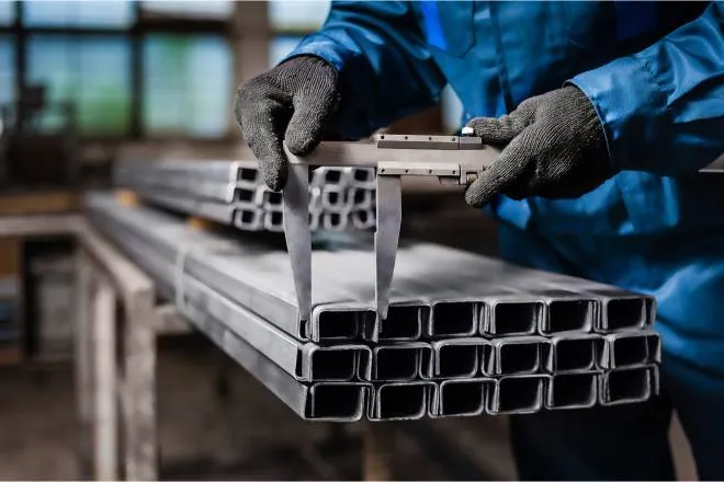 A professional metal fabricator wearing safety gloves as they lay freshly cut metal on a stack of other metal pieces.