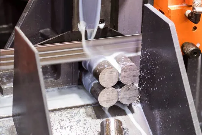 An orange saw cuts four steel rods as creamy-looking liquid streams down over the rods and flows down a silver chute.