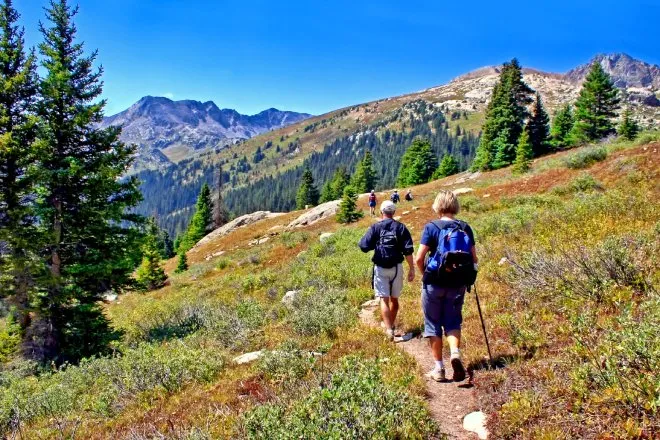 A man and woman walking through a path on Colorado's Lost Man Trail in the mountains wearing backpacks.