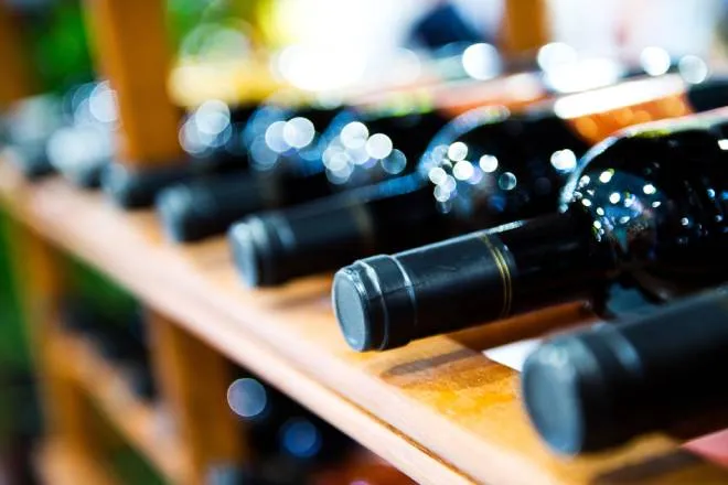 An extreme close-up view shows several dark-colored wine bottles lying on a wooden wine storage rack.