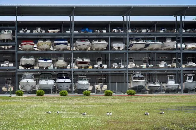 A large, open steel structure contains three shelf levels. Boats of different sizes and types sit on the various shelves.