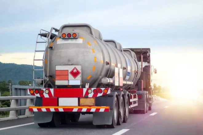 A large industrial truck driving on a road transporting flammable chemicals in a large cylindrical metal tank.