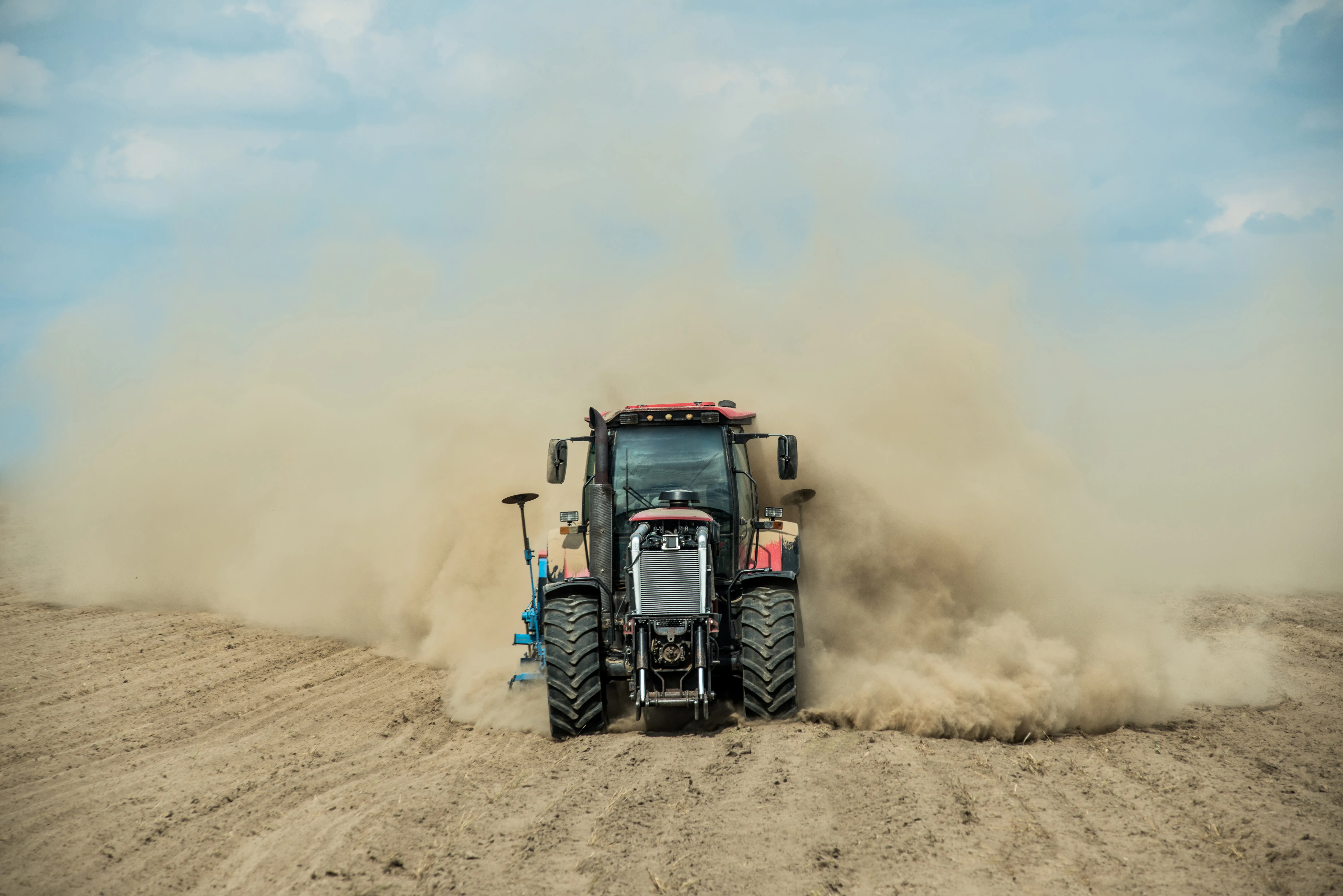 Farm tractor driving through bare dirt creating a dust cloud.