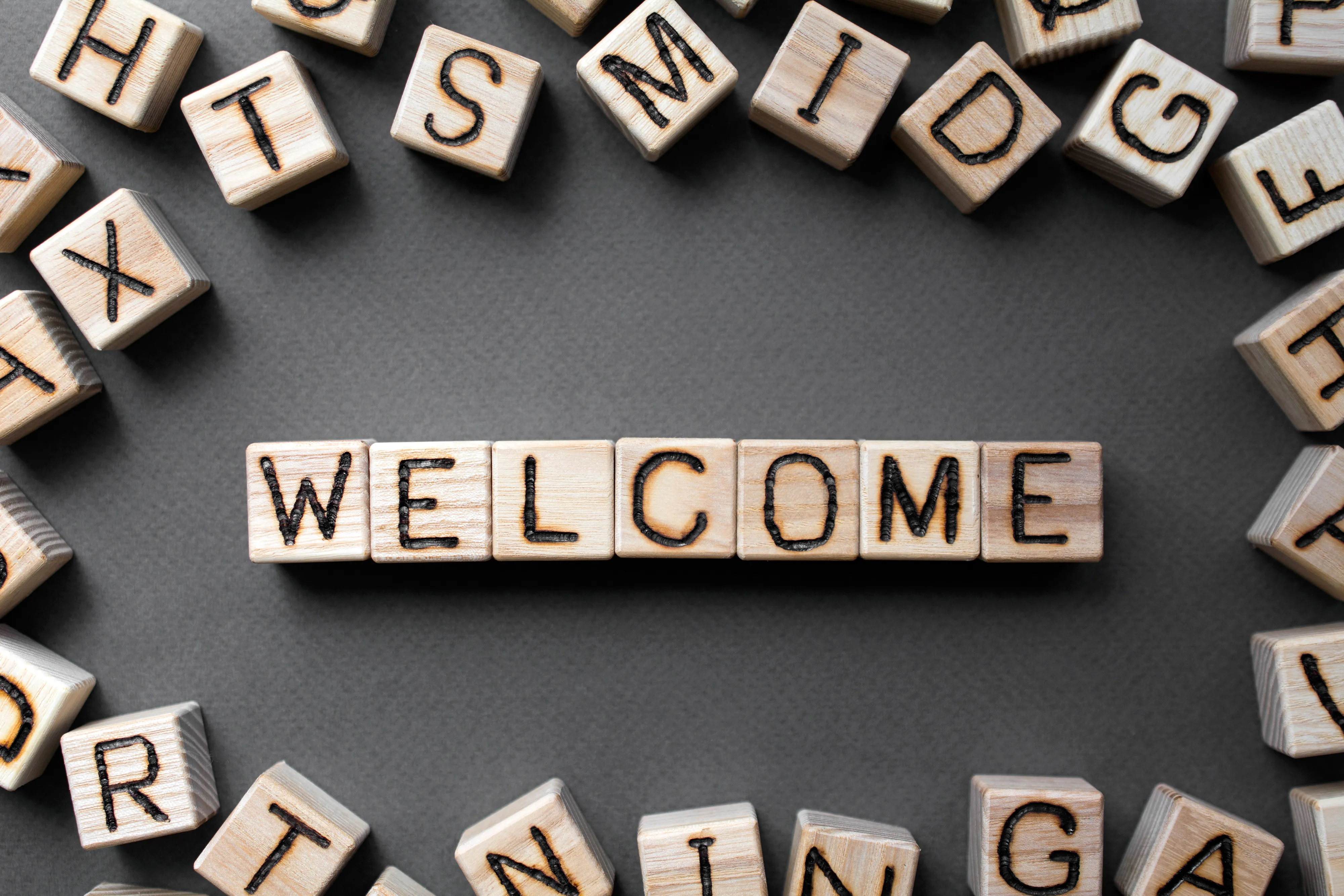 Assorted wooden blocks with letters on the side, surrounding wooden blocks spelling the word "welcome"