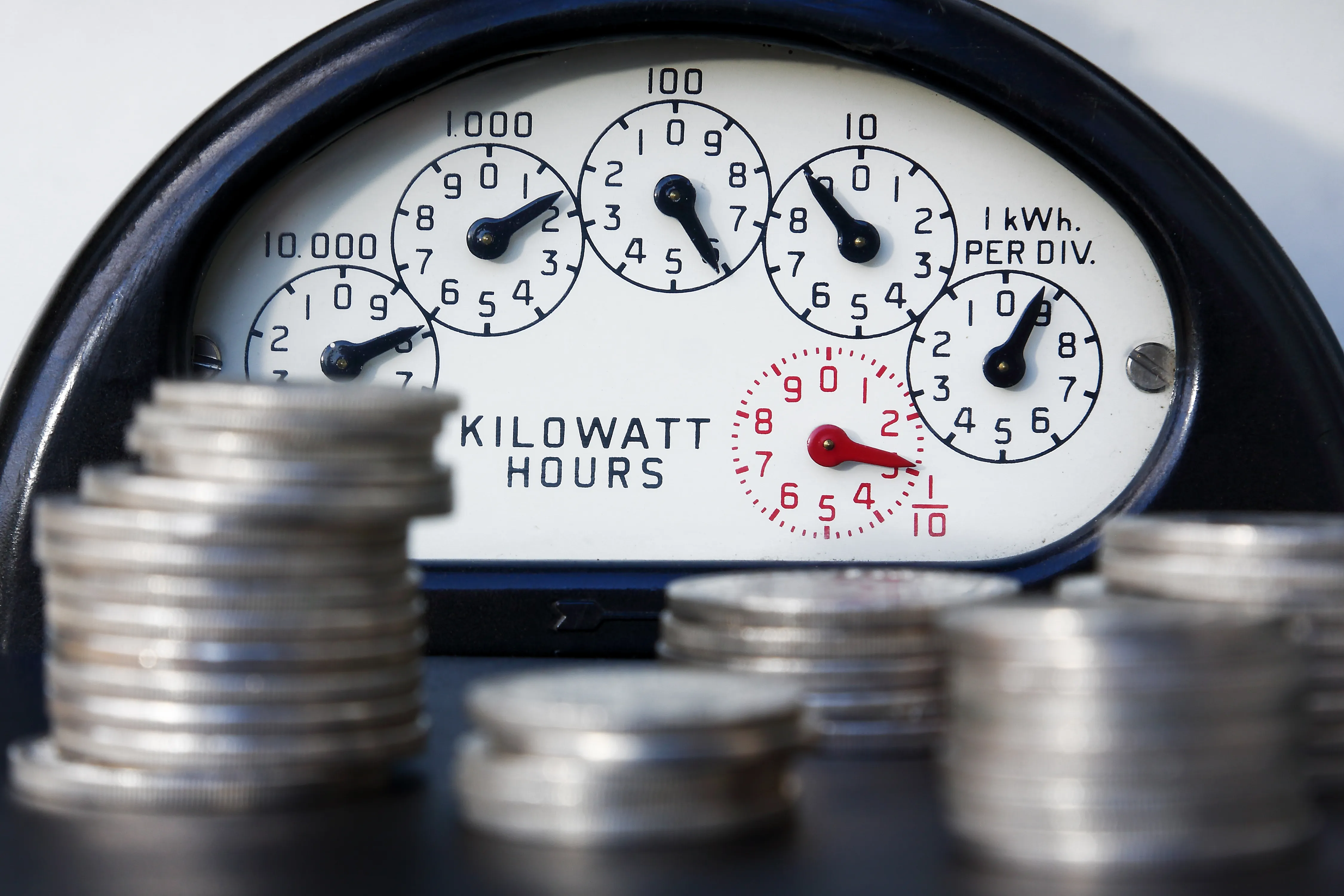 Dials on a electric meter with stacks of coins in front.