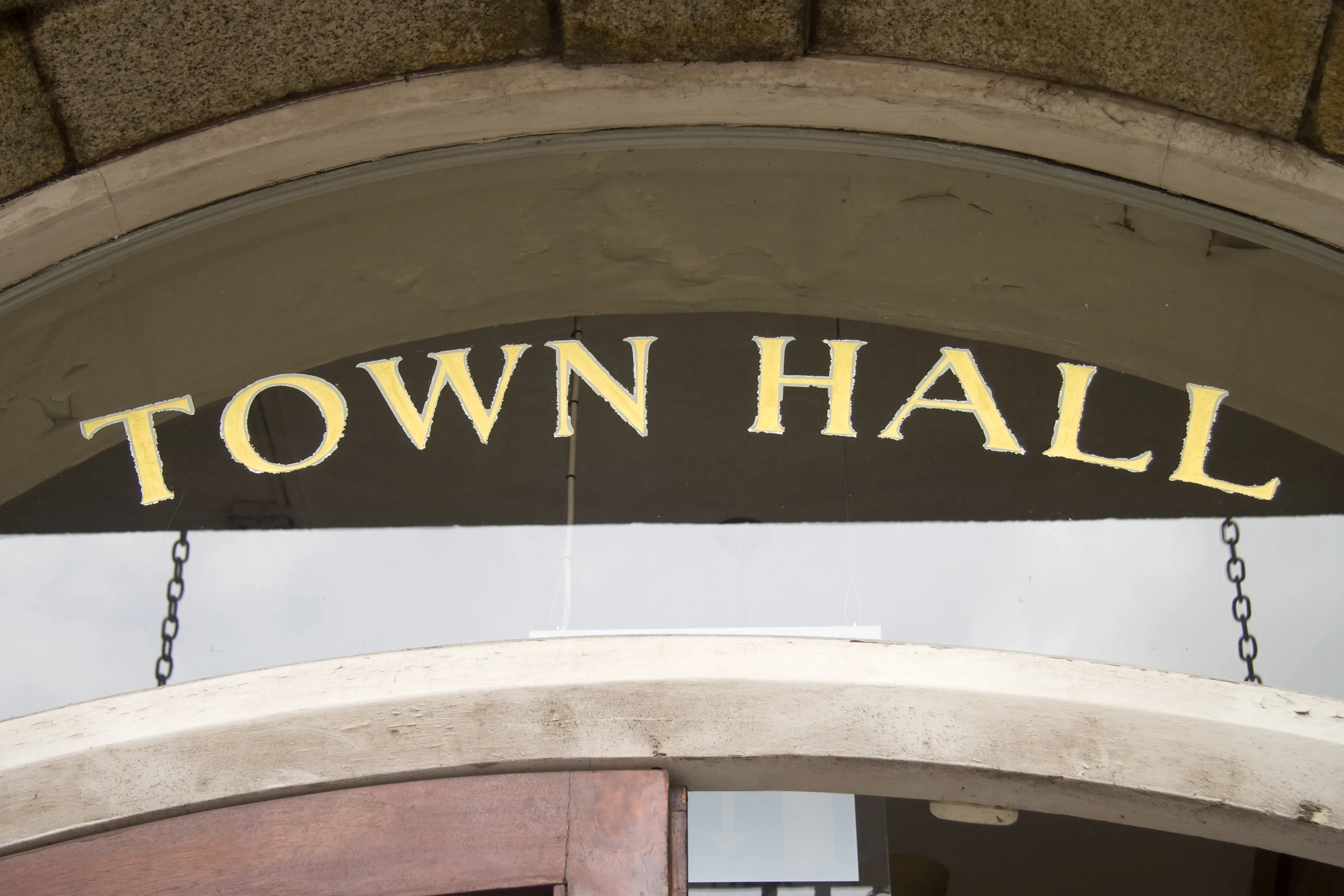 Close up of a door to a building with a glass transom above. The words "Town Hall" are stenciled on the glass in gold leaf foil.