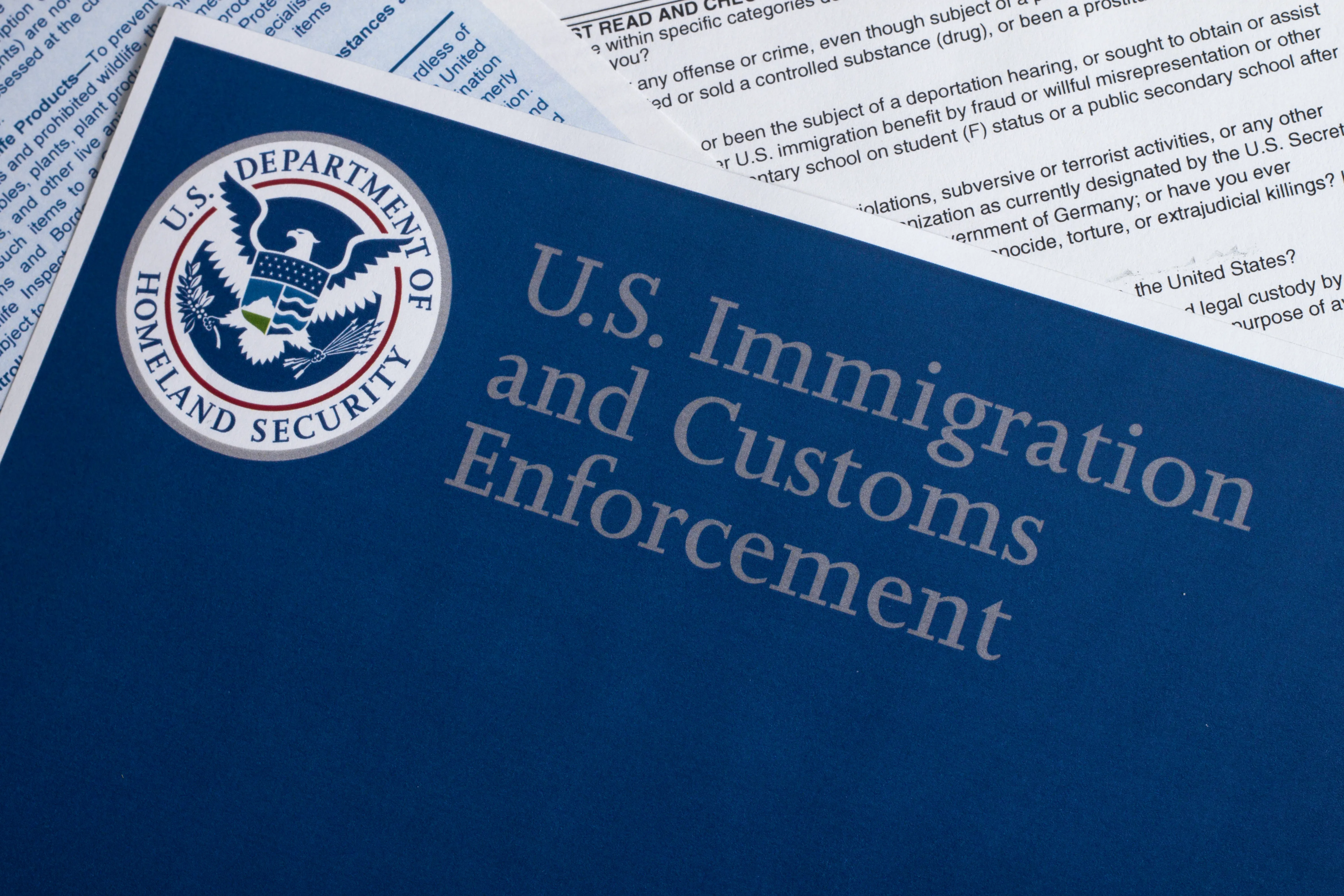 Overhead closeup of documents. The top document is entitled "U.S. Immigration and Customs Enforcement" with the United States Department of Homeland Security logo.