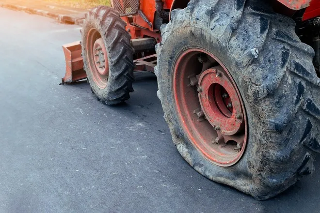 A red tractor sitting on the side of a paved road with a blown out rear tire and damaged rubber visible on the wheel.