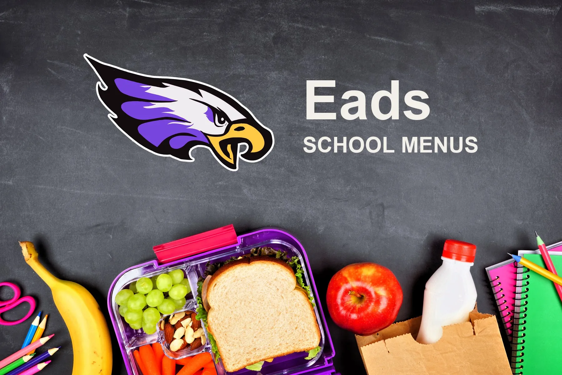 The Eads School Eagles mascot, chalked on a blackboard above a packed school lunch of a sandwich, grapes, carrots, an apple and a bottle of milk, with pencils and notebooks. The board reads “Eads School Menus”.