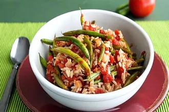 Bowl of green bean and rice casserole sitting on a place next to a spoon.