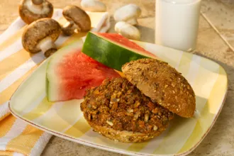 Plate with mushroom beef sloppy Joe filling on a bun next to a slice of water melon.