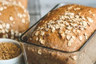 Loaf of oatmeal bread in a pan next to a bowl of unprocessed oats.