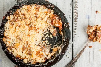 Plate of Peach Apple Crisp next to a spoon on painted wood surface.