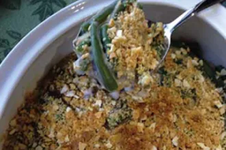 Serving bowl of green bean casserole with spoonful held above.