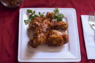 Square plate with pieces of spicy southern barbecue chicken on a wood table next to a fork on a napkin.