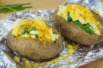 Two spinach stuffed potatoes on a sheet of foil.