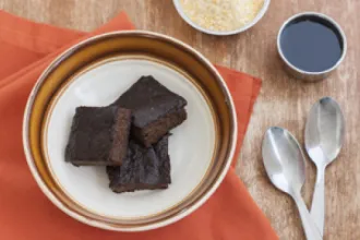 Bowl on a placemat next to two spoons with three portions of Sweet Cornmeal Pudding with Ginger and Cinnamon