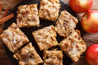 Plate of apple cinnamon bars next to fresh apples and cinnamon sticks.