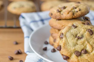 Plate of chocolate chip yogurt cookies on a dish towel, next to a few individual chocolate chips and a wire cooling rack of cookies.