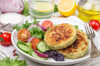 Plate with a fork, two walleye patties and an assortment of fresh vegetables, surrounded by fresh vegetables and fruit.