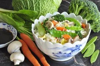 Bowl of fried rice, topped with, and surrounded by, fresh vegetables.