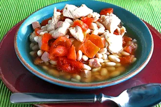 Bowl of Great Norther bean soup on a plate next to a spoon.