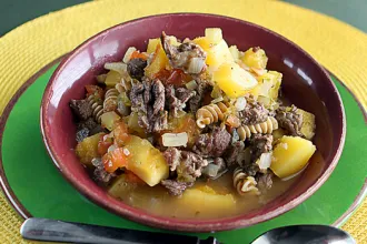 Bowl of hearty beef soup on a plate next to a spoon.