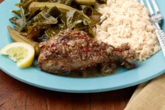 Plate with Jamaican Jerk Chicken, rice, cooked greens, and a lemon wedge.