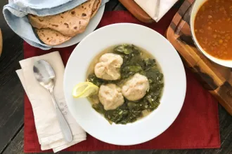 Bowl of Kibbeh Khamoustah next to a spoon and napkins. A nearby cloth holds flat bread.