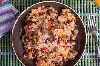 Plate containing vegetables and rice on a mat next to a fork and cloth.