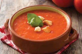 Bowl of tomato basil soup on a cloth, sitting on a wood surface.