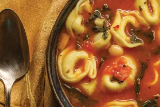 Close up of a bowl of tortellini soup next to a spoon