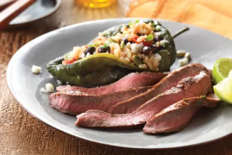 Plate with slices of lime-marinated flank steak next to a stuffed Poblano pepper and lime wedges