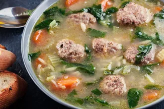 Overhead image of a bowl of meatball soup next to a spoon.