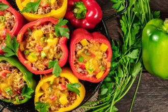 Serving dish of peppers stuffed with rice and beans next to a whole green bell pepper and bundle of cilantro.